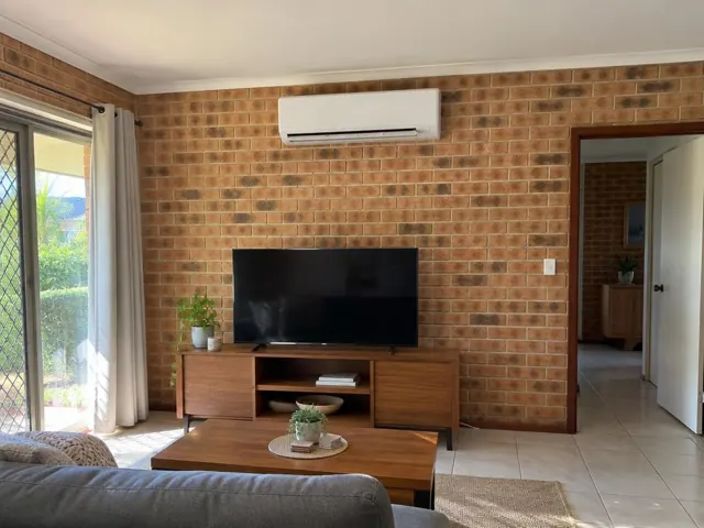 Wall-mounted split system above a TV on a brick feature wall in a living room in Arundel